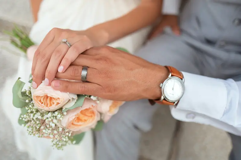 A couple holding hands over a wedding bouquet of pale peach and white flowers