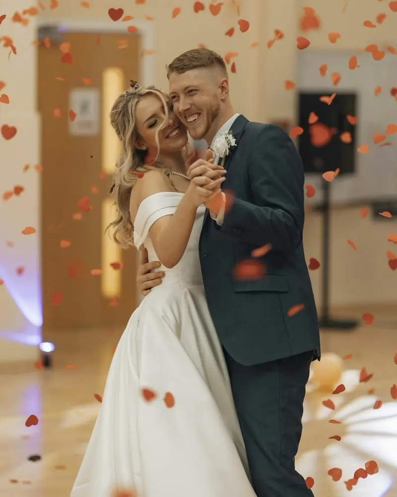 Newlyweds dancing together beneath red confetti