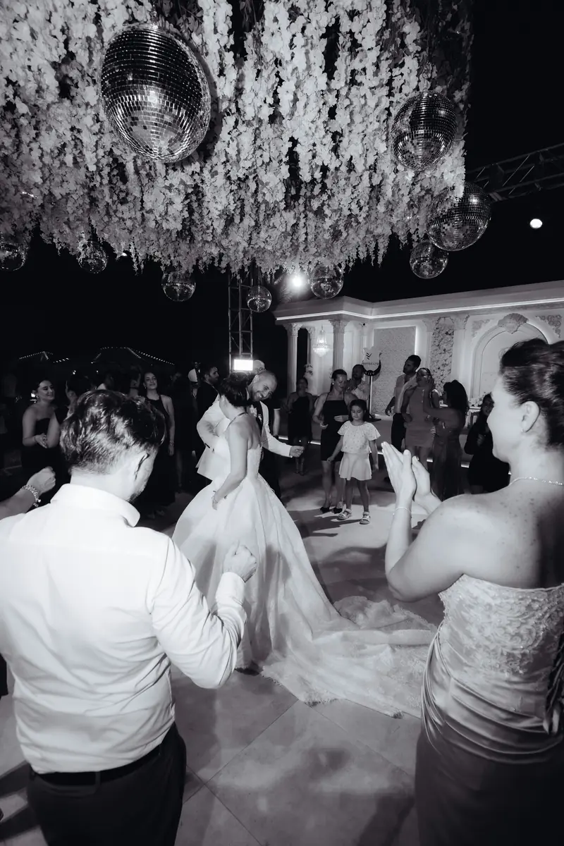 Newlyweds dancing with guests beneath flowers and mirrored disco balls