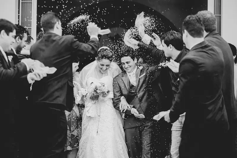 Newlyweds laughing as guests shower them with confetti in black and white
