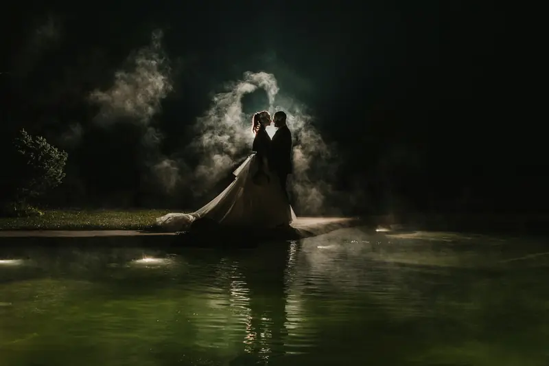 Wedding couple beside a pool in dramatic backlit evening mist