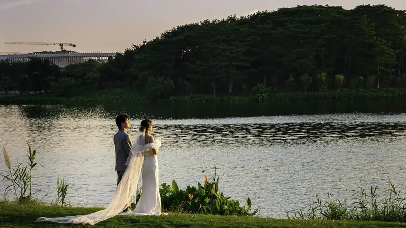 Bride and groom standing together beside a lake in evening light